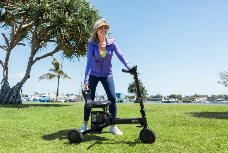 Woman standing with an Igofor folding mobility scooter in a waterside park